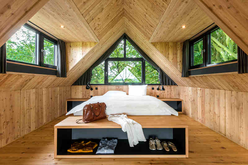 Blick in den großzügigen Schlafbereich der Lütetsburg Lodges in Ostfriesland. deren modernes Design typisch für viele Baumhaushotels in Niedersachsen ist. 