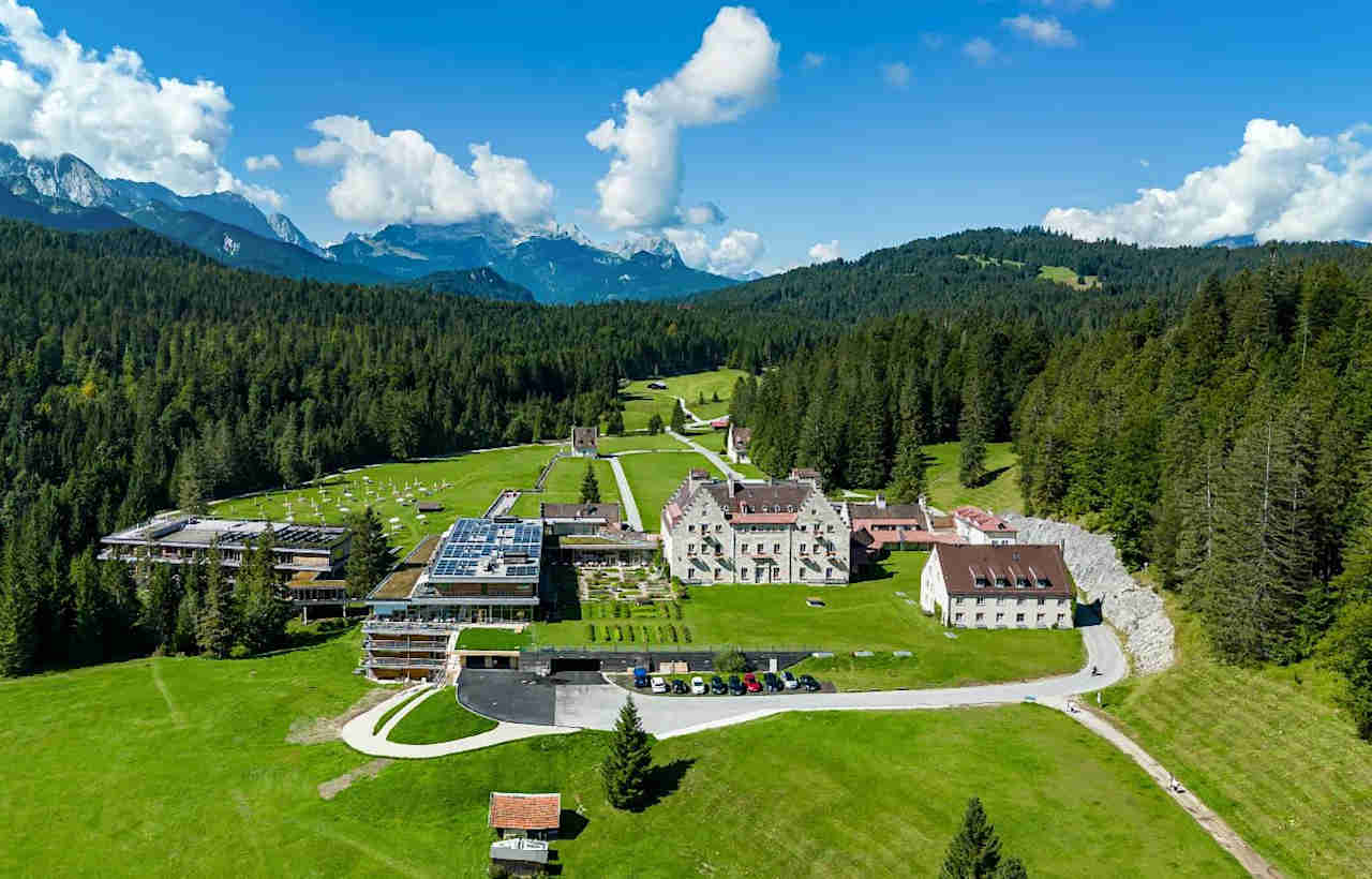Die Luftaufnahme zeigt das Kranzbach Hotel mit Badehaus und dem angebauten Gartenflügel von oben (mit Blick ins Elmauer Tal).