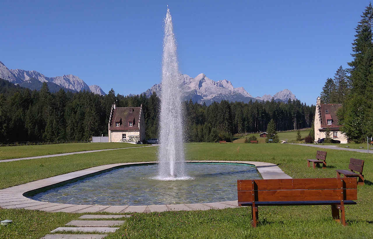 Die imposante Wasserfontäne vor dem Naturhotel Das Kranzbach ist ein unerwarteter Anblick vor der Bergkulisse am Fuße der Zugspitze.